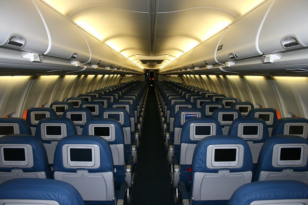 Cabine d'avion vide, rangées de sièges bleus vues depuis l'allée centrale.